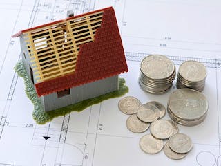 Hausbau-Modell auf Grundrissplan mit Münzen