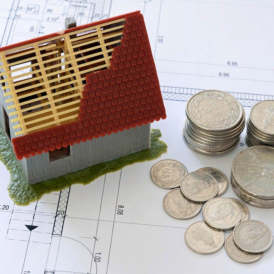 Hausbau-Modell auf Grundrissplan mit Münzen