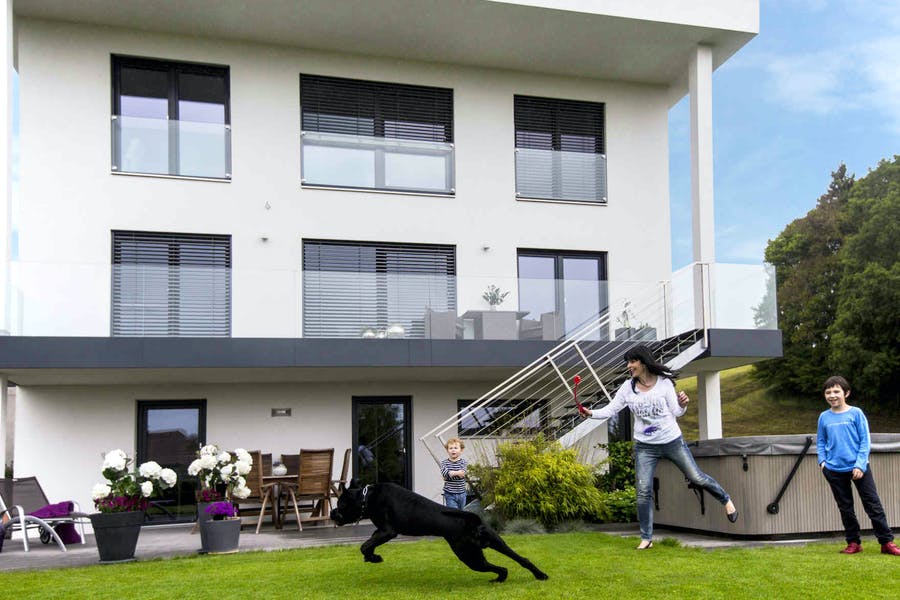 Familie spielt vor ihrem weißen VARIO-HAUS mit einem schwarzen Hund