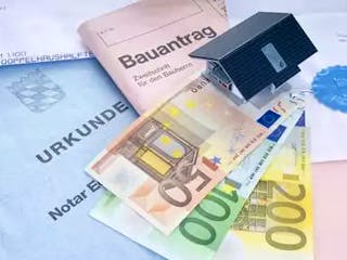 Hausmodell auf Notarurkunde und Geldscheinen